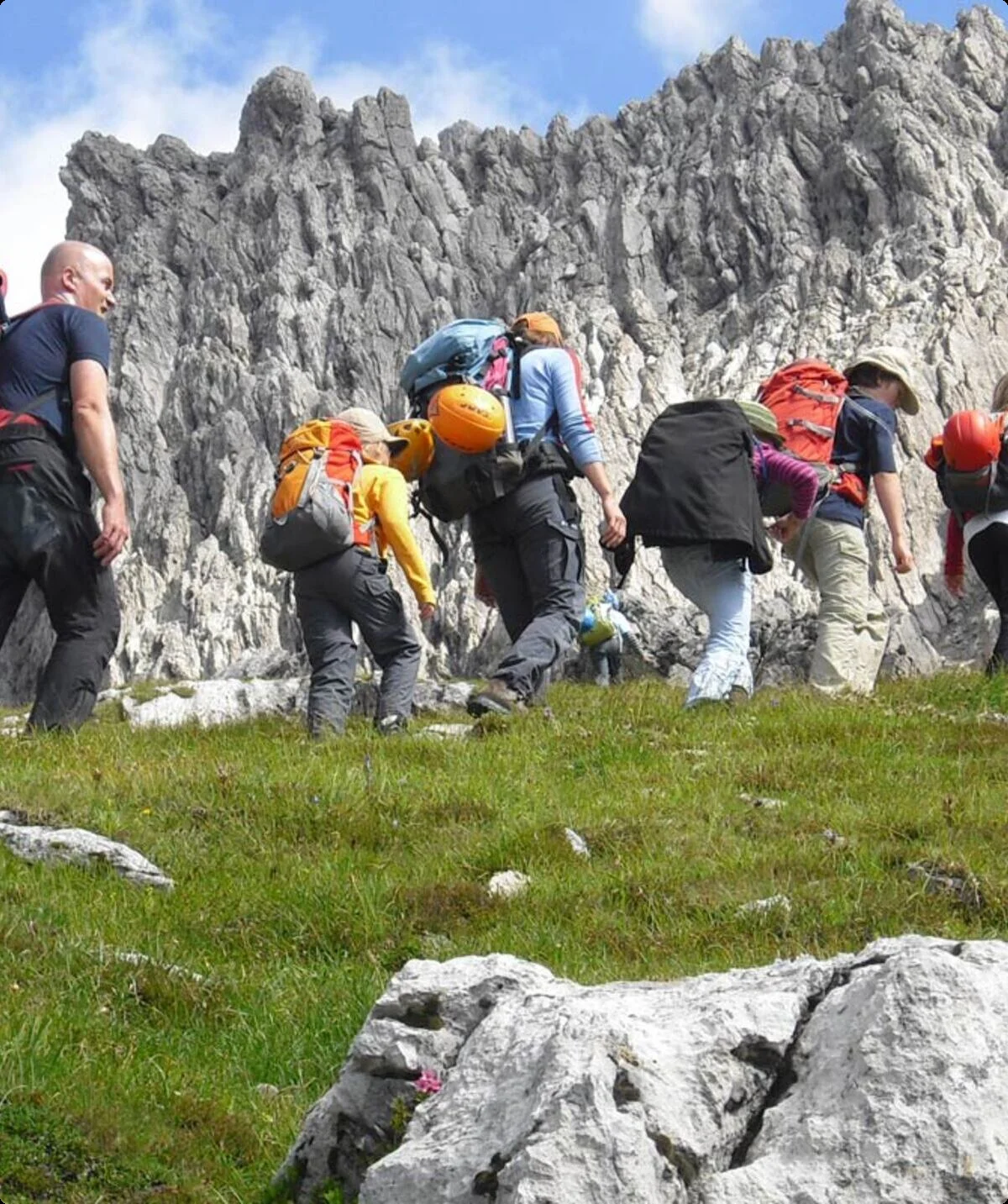 Es wird gewandert bei sonnigen Wetter auf einer Art Wiese, Im Hintergrund steile Felswände | © DAV Münster