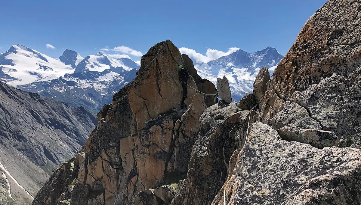 Im Hintergrund sind viele schneebedeckte Berge zu sehen. Im Vordergrund sieht man entfernt einen Kletterer an einem Sicherungsseil. | © DAV Münster