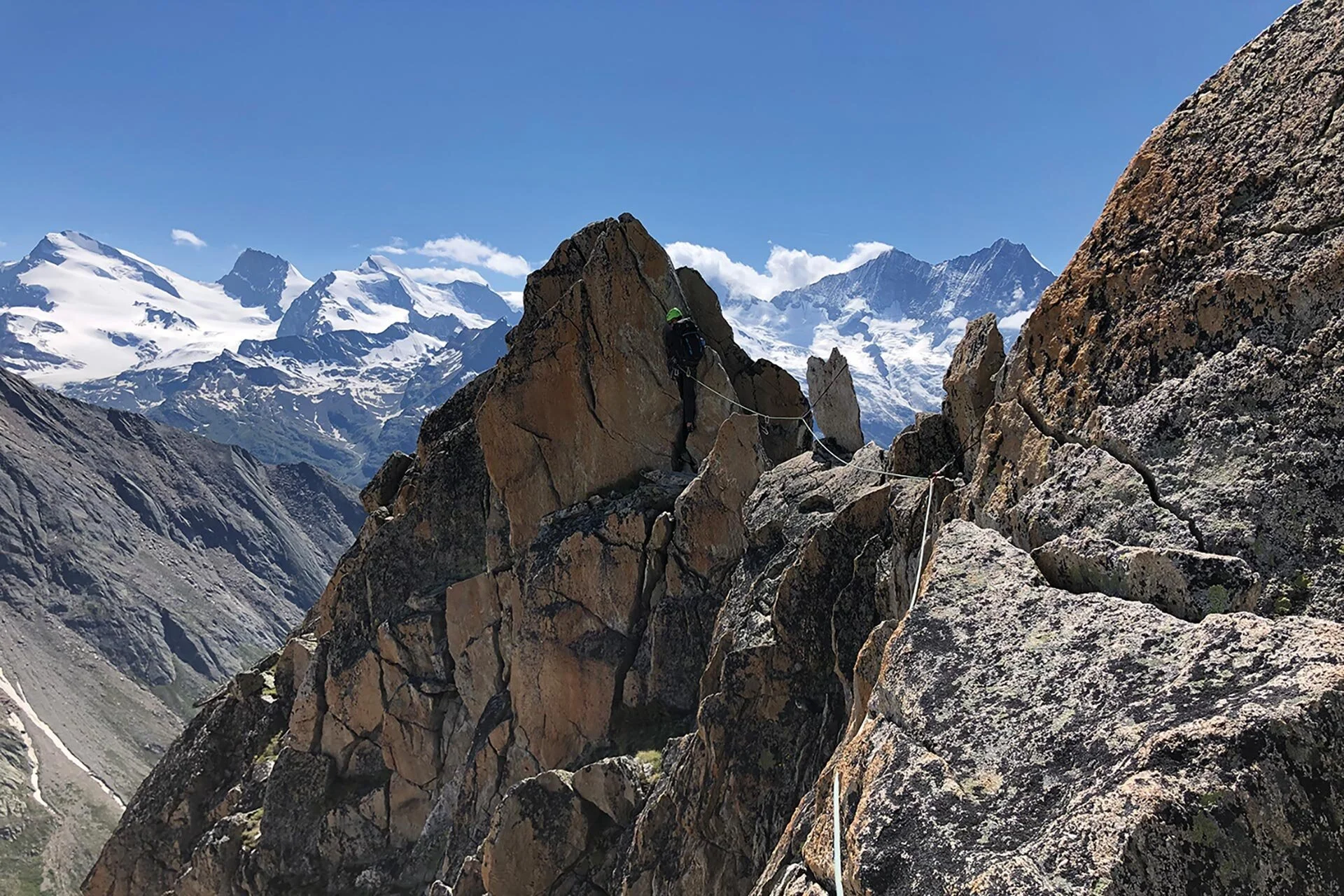 Im Hintergrund sind viele schneebedeckte Berge zu sehen. Im Vordergrund sieht man entfernt einen Kletterer an einem Sicherungsseil. | © DAV Münster