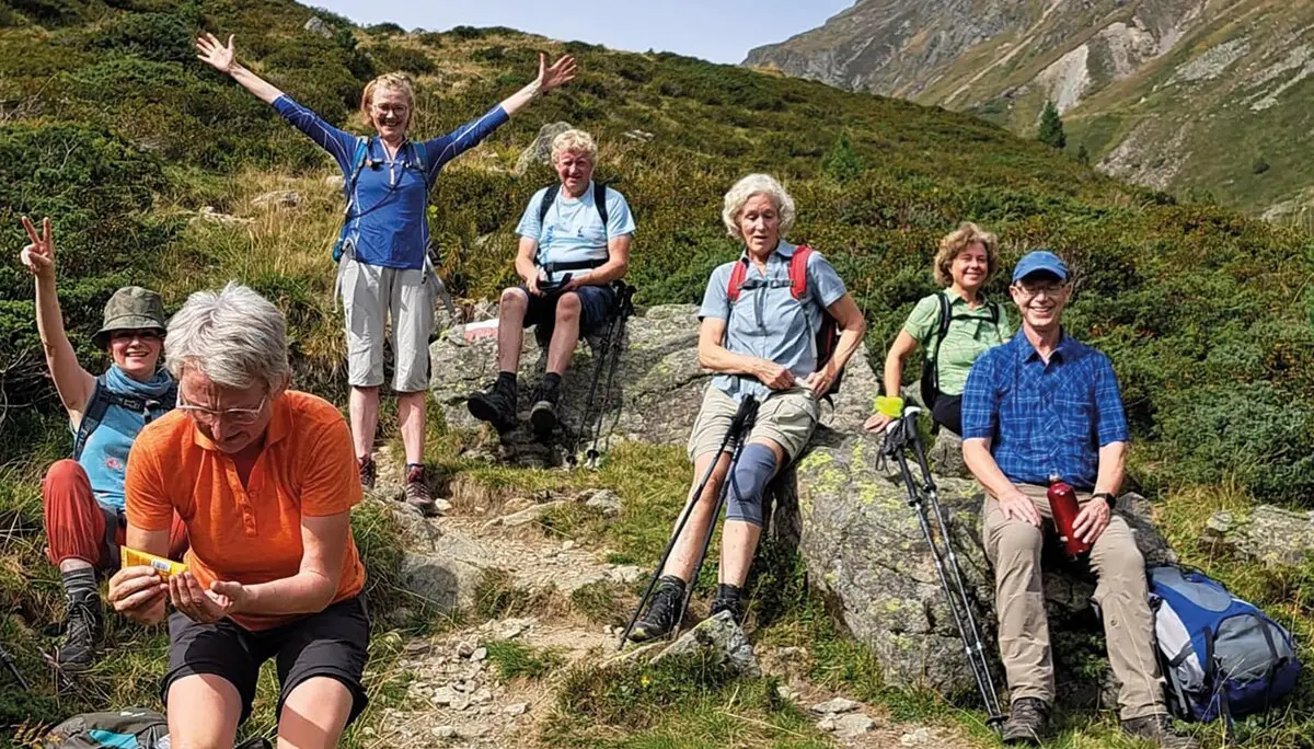 Es sind sieben Wanderer in den Bergen zu sehen die eine Pause machen.  Sechs sitzen z.B. auf Steinen, eine steht aufrecht und hat die Hände nach oben gestreckt. Im Hintergrund sind Berge zu erahnen.  | © DAV Münster