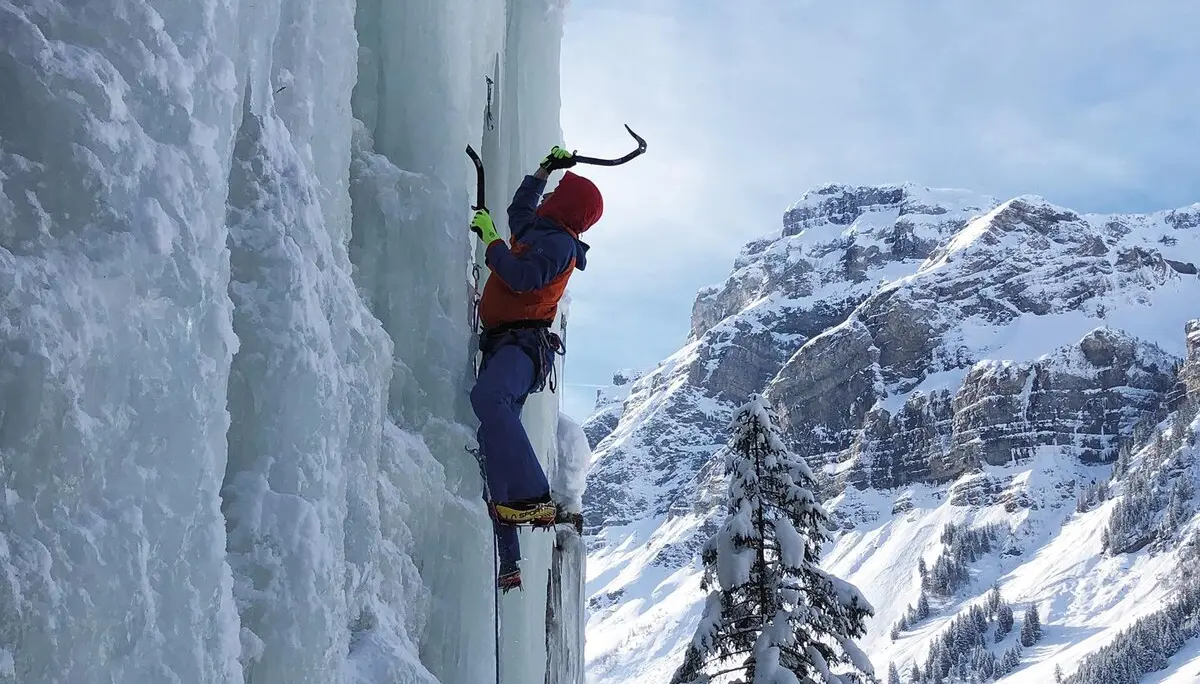 Es ist ein Eiskletterer in einer senkrechten Eiswand zu sehen, rechts daneben ist ein schöner Berg zu sehen | © DAV Münster