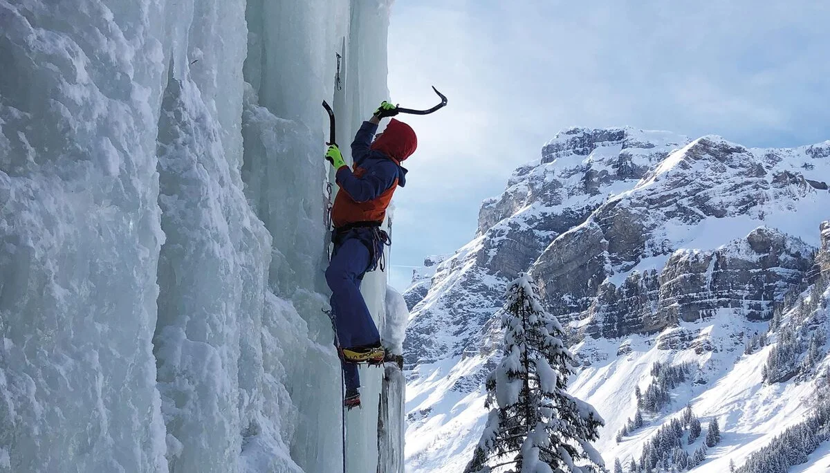 Es ist ein Eiskletterer in einer senkrechten Eiswand zu sehen, rechts daneben ist ein schöner Berg zu sehen | © DAV Münster