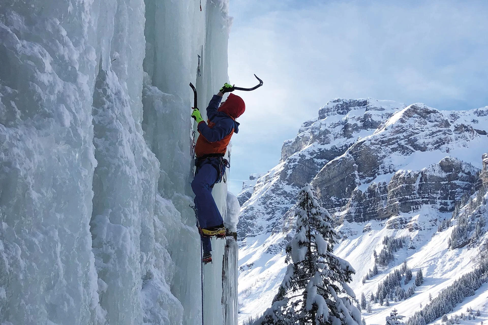 Es ist ein Eiskletterer in einer senkrechten Eiswand zu sehen, rechts daneben ist ein schöner Berg zu sehen | © DAV Münster