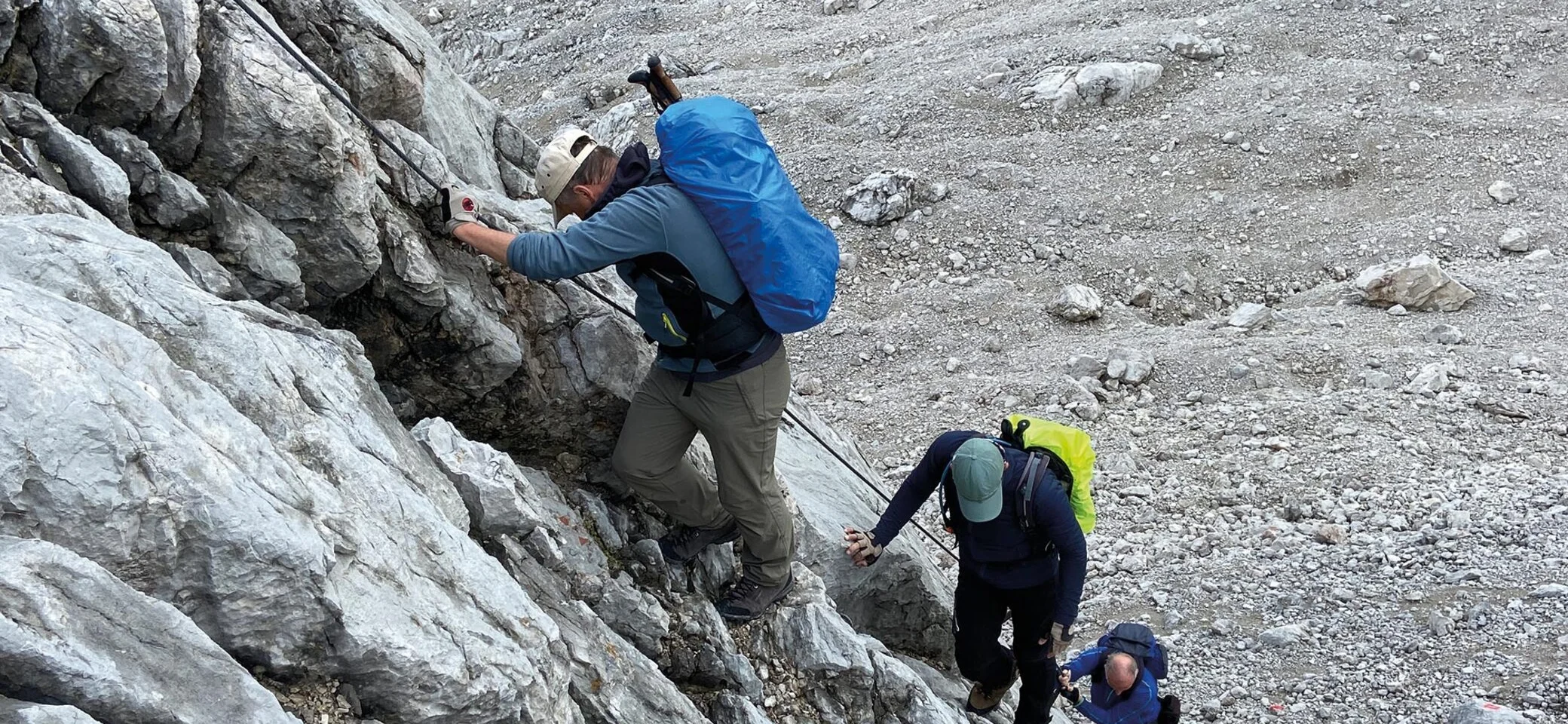 Es sind drei Wanderer mit Rucksäcken zu sehen, die an einem Sicherungsseil nach oben klettern. Alle schauen nach unten oder zur Seite. | © DAV Münster
