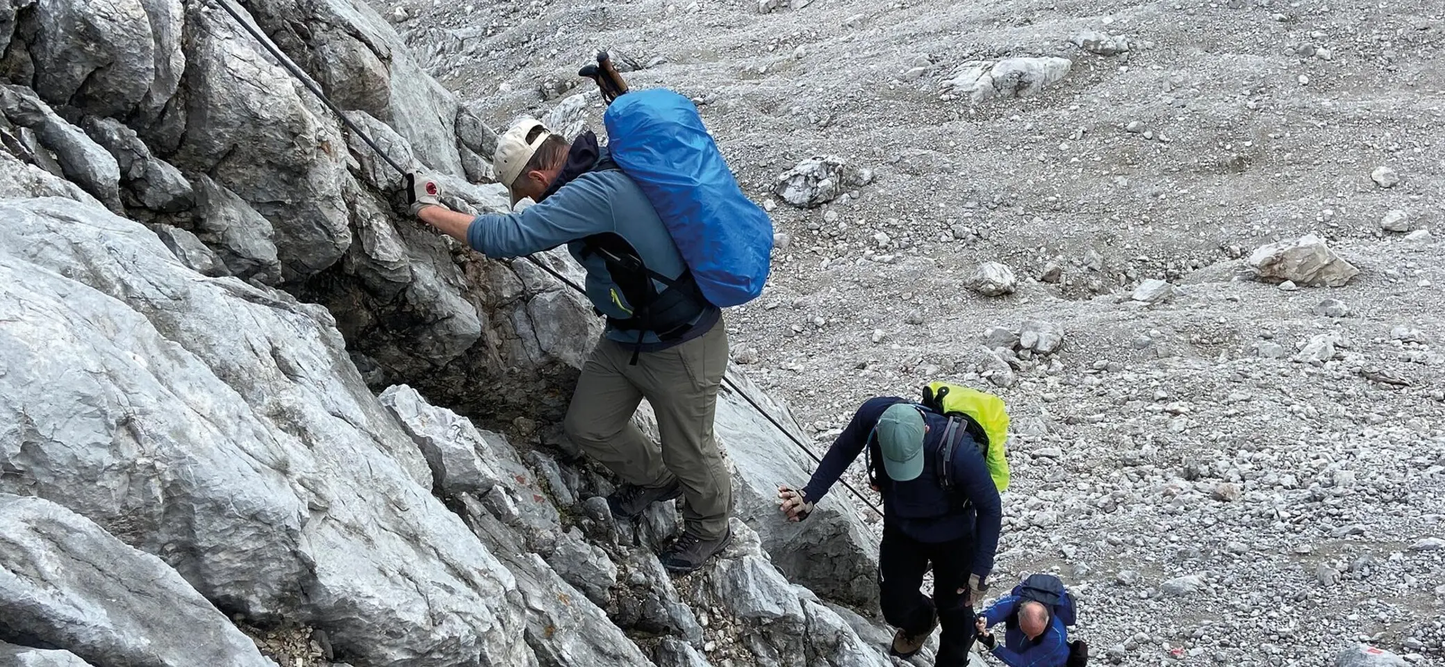 Es sind drei Wanderer mit Rucksäcken zu sehen, die an einem Sicherungsseil nach oben klettern. Alle schauen nach unten oder zur Seite. | © DAV Münster