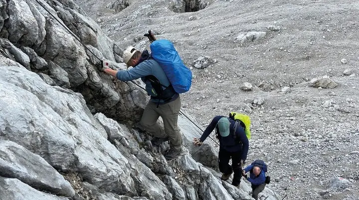 Es sind drei Wanderer mit Rucksäcken zu sehen, die an einem Sicherungsseil nach oben klettern. Alle schauen nach unten oder zur Seite. | © DAV Münster