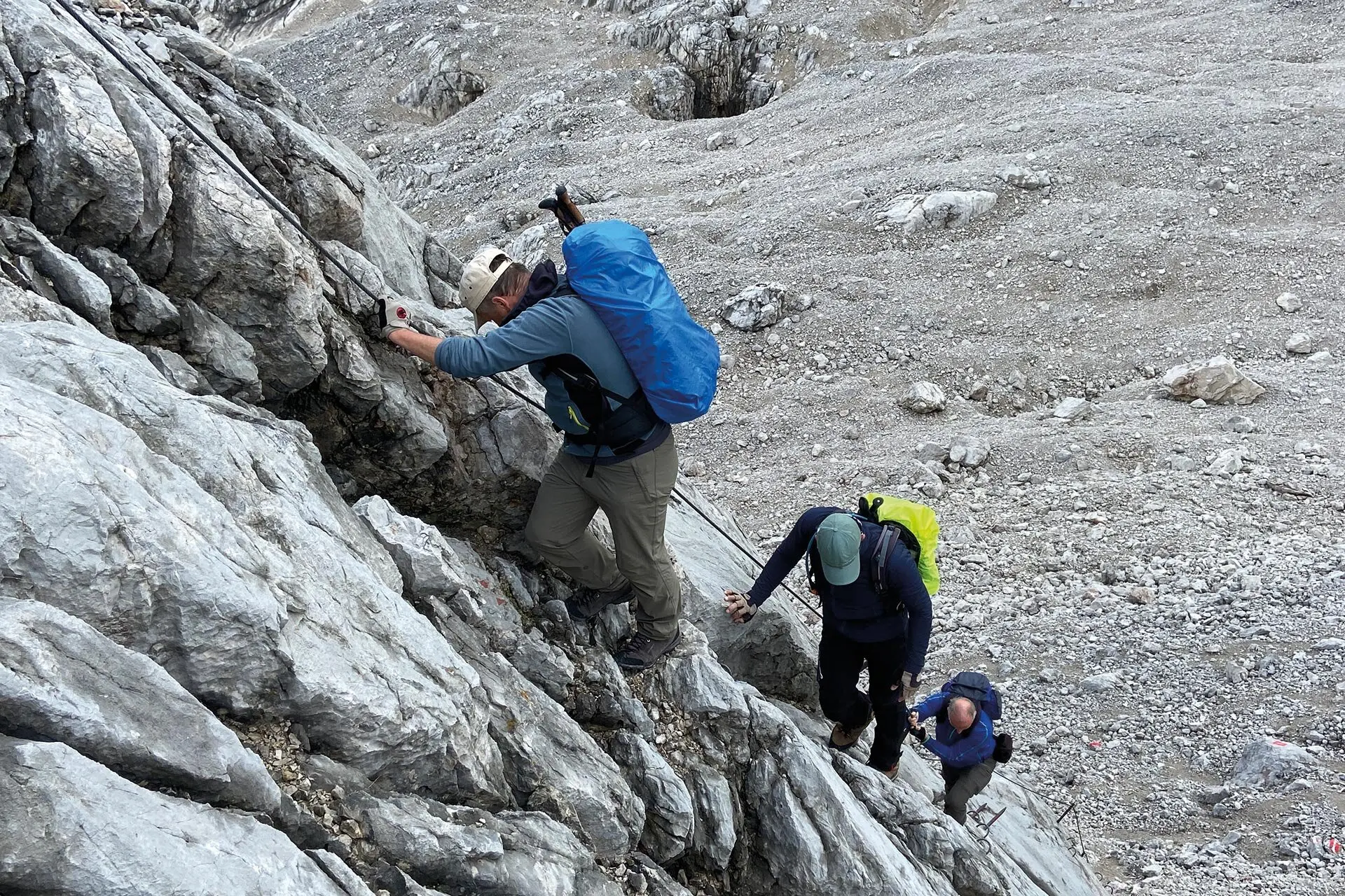 Es sind drei Wanderer mit Rucksäcken zu sehen, die an einem Sicherungsseil nach oben klettern. Alle schauen nach unten oder zur Seite. | © DAV Münster