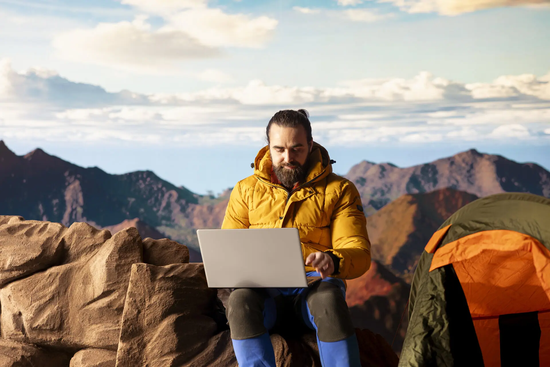 Mann ist mit Laptop neben Zelt auf einer Bergkette beschäftigt | © Freepic.com